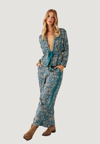 Blusa y pantalones de color teal con estampado floral, con cintura ajustable, mangas largas y rayas laterales. Combinados con botines marrones.