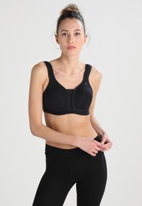 Soutien-gorge de sport noir avec larges bretelles, bonnets moulés et texture lisse. Associé à des leggings noirs taille haute, mettant en valeur une coupe ajustée.