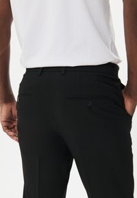 Svarta byxor med en slät textur, slim fit, två bakfickor med knappstängning och en midja med bältes-hål.