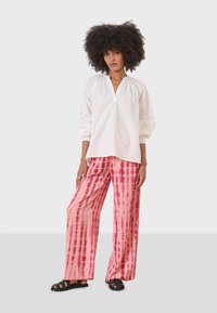 White, woven blouse with a V-neck and gathered sleeves, paired with loose, pink tie-dyed pants featuring vertical stripes. Black sandals.