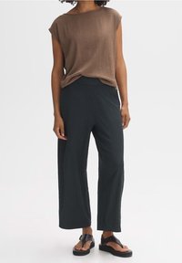 Brun texturerad kortärmad topp kombinerad med mörkgröna vida byxor. Modellen bär svarta platta sandaler. Enkel och modern design.