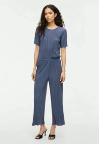 Námornícky modrý plisovaný dvojdielny outfit so svetlom predným topom a širokými nohavicami. Hladká textúra, elastický pás a minimalistický dizajn.