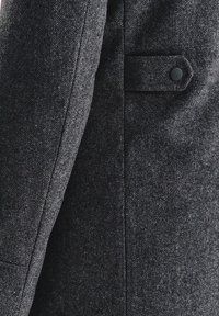 Szary żakiet w jodełkę o gładkiej fakturze, z uporządkowanym krojem, skośnym klapem oraz pojedynczym guzikiem na przedniej kieszeni.