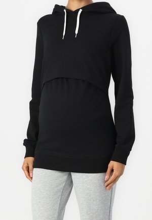 Schwarzer Umstands-Hoodie mit langen Ärmeln und weißen Kordeln, getragen mit hellgrauen Jogginghosen, gezeigt von den Schultern bis zur Mitte des Oberschenkels.
