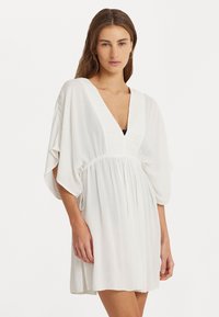 Vestido blanco con escote en V profundo, mangas cortas tipo murciélago y cintura fruncida. Fabricado en un material ligero y fluido con un acabado texturizado.