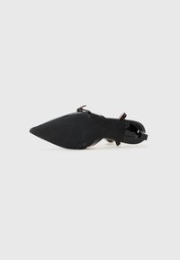 Scarpa nera in vernice con tacco alto, punta affilata e cinturino alla caviglia, caratterizzata da una suola testurizzata e un finish lucido.