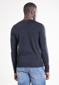 Ciemnogranatowy sweter z dzianiny, z okrągłym dekoltem i ściągaczami na rękawach. W połączeniu z jasnoniebieskimi jeansami.