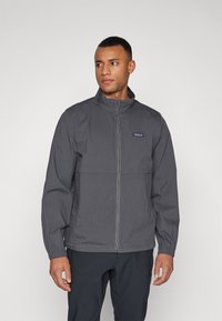 Gray zip-up jacket with a high collar, features elastic cuffs and a simple design. Logo patch displayed on the left chest area.
