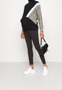 Zwart-wit gekleurde sweatshirt met luipaardprint mouwen, gecombineerd met donkerbruine leggings en witte sneakers; met een zwarte handtas.