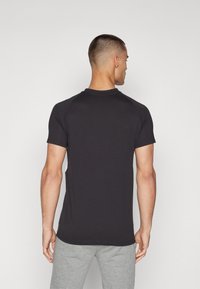 Tricou negru cu mânecă scurtă, dintr-un amestec de bumbac, cu guler rotund și mâneci raglan, asortat cu pantaloni sport gri.