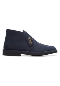 Bota desierto de ante azul marino con punta redonda, parte delantera con cordones y suela de goma negra; cuenta con una etiqueta de logo dorado y detalles de costura.