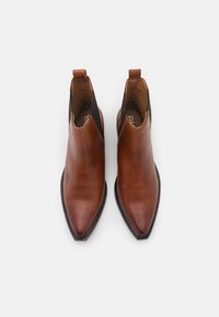 Bottines en cuir marron avec un bout pointu, des panneaux latéraux élastiques noirs, et une languette à l'arrière. Texture lisse avec un design épuré.