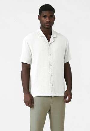 Kortærmet, hvid tekstureret skjorte med knapper foran og åben krave, kombineret med lysegrønne bukser med lignende struktur.