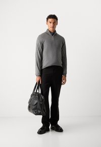 Gray zip-up sweater, black trousers, holding a black leather bag. The outfit features a textured fabric and simple design. Shoes are black.