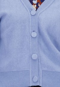 Lichtblauwe gebreide cardigan met bijpassende stofbedekte knopen en ribgebreide randen, gedragen over een patroonstuk.