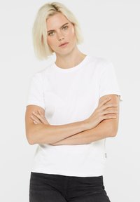 White cotton t-shirt with short sleeves, round neck, and a straight cut. Accented with a small label on the left side. Pairing with dark jeans.