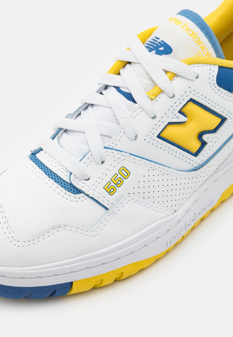 Weiße Ledersneaker mit blauen und gelben Akzenten, ausgestattet mit perforierten Details, robusten Schnürsenkeln und einer auffälligen "550"-Markierung an der Seite.
