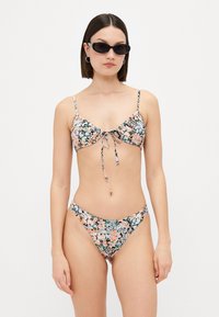 Blommig bikiniuppsättning med svart bakgrund och rosa samt gröna blommor, justerbar knyt framtill på toppen och matchande låga badbyxor.