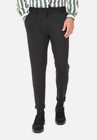 Czarne zwężane spodnie z miękkiego materiału, z sznurkiem w pasie, bocznymi kieszeniami i podwijanymi mankietami. Noszone z czarnymi butami.