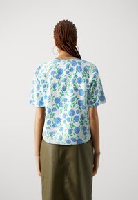 Hvit kortermet topp med blå blomstermønster og grønne blader, med en avrundet nederkant. Kombinert med en ensfarget grønn skjørt.