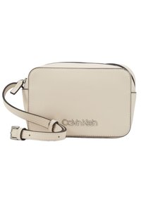 Beżowa torebka crossbody Calvin Klein z gładkiej skóry, prostokątny kształt, zamek błyskawiczny oraz regulowany pasek. Posiada akcenty z logo.