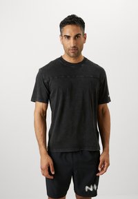 Schwarzes Baumwoll-T-Shirt mit Rundhalsausschnitt, kurzen Ärmeln und einer horizontalen Nahtdetails über der Brust. Minimalistisches Logo auf der linken Seite.