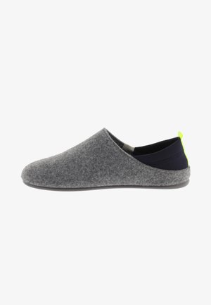 Zapato gris tipo slip-on con un talón de tela negra y una pequeña pestaña de acento en neón verde; presenta una textura suave y una punta redondeada.