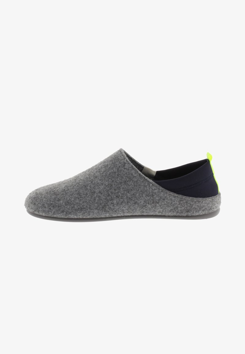 Zapato gris tipo slip-on con un talón de tela negra y una pequeña pestaña de acento en neón verde; presenta una textura suave y una punta redondeada.
