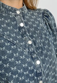 Koszula jeansowa z motywem motyli, jasnoniebieska i biała, ze stójką, zapięciem na guziki z przodu oraz bufkami na rękawach o subtelnej fakturze.