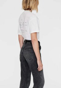 Hvid kortærmet T-shirt med trykt tekst på ryggen, parret med højtaljede, løse mørkegrå jeans.