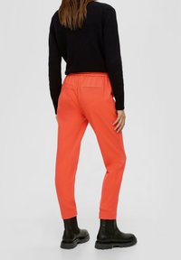 Orangene Jogginghosen mit elastischem Bund und schmalem Schnitt, ausgestattet mit zwei Gesäßtaschen und gerippten Bündchen, kombiniert mit schwarzen Knöchelboots.