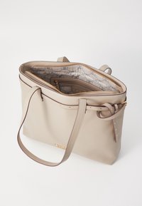 Sac fourre-tout en similicuir beige avec deux longues anses, quincaillerie dorée et compartiment principal zippé. L'intérieur est doté d'une doublure à motif.