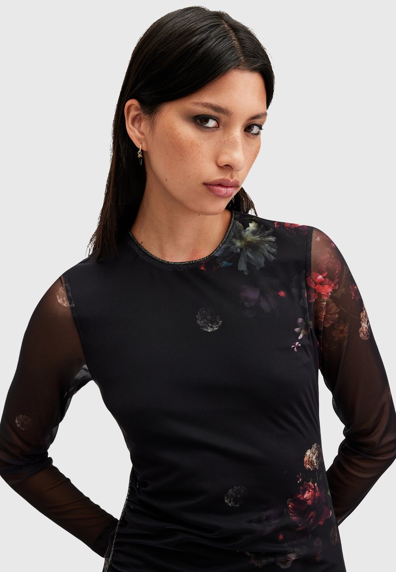 Top negro de mangas largas con estampado floral, mangas de malla semitransparente, cuello redondo y silueta ajustada con un ligero brillo.