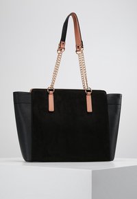 Musta olkalaukku, jossa on samettinen etupinta ja tekstuuriset mustat sivut. Varustettu ruusukultaisilla ketjuhihnoilla ja nahka yksityiskohdilla. Rakenteellinen muotoilu.