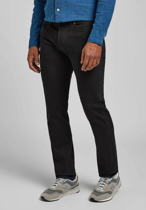 Jeans negros con corte slim, fabricados en denim, combinados con zapatillas grises. La camisa es de color azul con un patrón texturizado y botones.