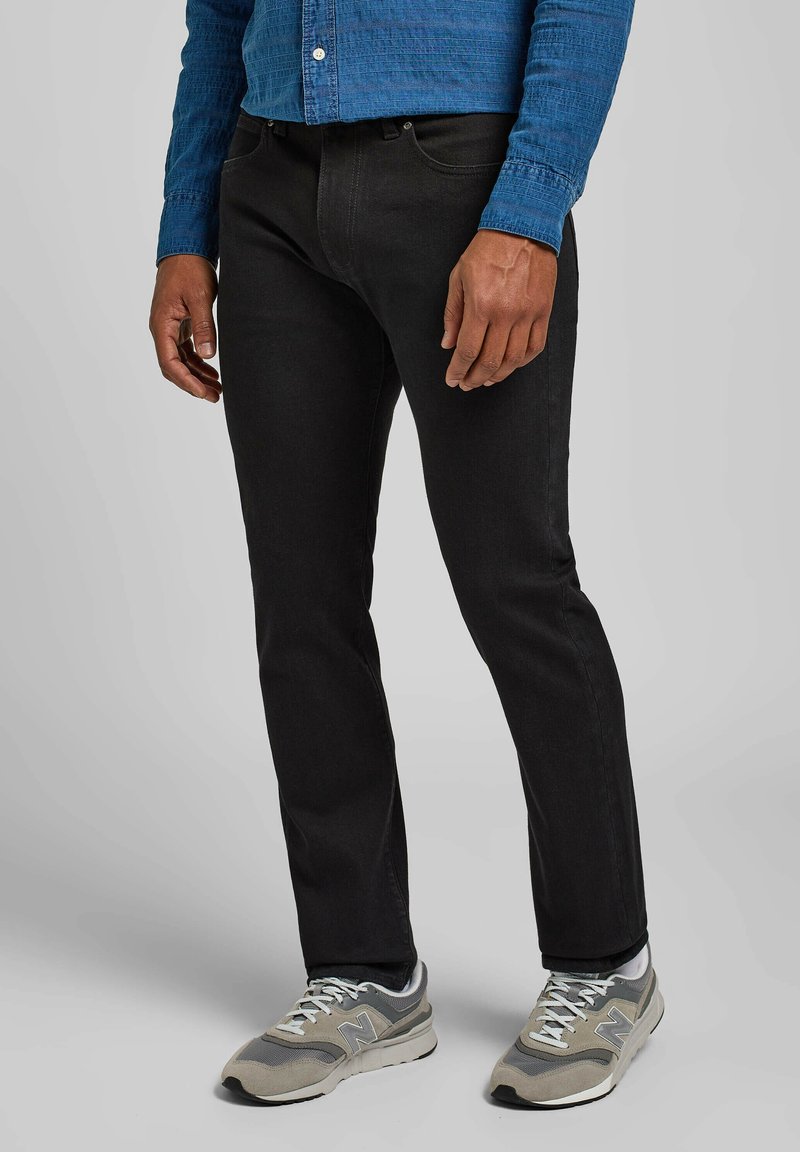 Jeans negros con corte slim, fabricados en denim, combinados con zapatillas grises. La camisa es de color azul con un patrón texturizado y botones.