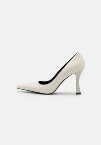 Hvide læder højhælede pumps med spidse tæer og et unikt vinklet hældesign. Har en glat tekstur og en sort indersøm.