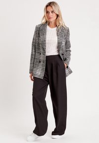 Gray and white plaid blazer with double buttons, paired with black wide-leg trousers and white sneakers. Textured knit top underneath.