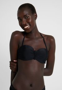 Zwarte bandeau bikini top met gevlochten detail in het midden en dunne verstelbare bandjes, gemaakt van gladde, rekbare stof.