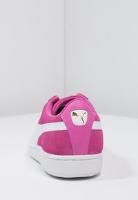 Baskets en daim rose avec accents blancs, dotées d'un col rembourré et d'un logo doré sur le talon, bout arrondi et semelle texturée.