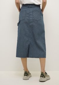 Falda midi de mezclilla con un patrón de rayas azul y blancas, con dos bolsillos traseros y una abertura frontal, combinada con zapatillas gruesas.