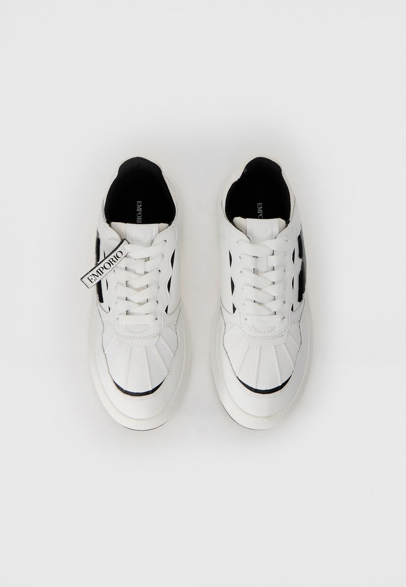 Sneakers bianchi con accenti neri, realizzati in materiale sintetico liscio. Presentano un design cucito, punta rotonda e lacci prominenti.