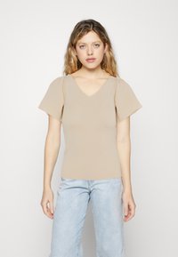 Beige V-hals topp med korte flared ermer, laget av mykt stoff. Kombinert med lyseblå jeans, med en avslappet passform og subtil fading.