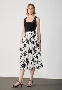 Débardeur noir à encolure carrée, associé à une jupe midi blanche à imprimé floral avec un design plissé. Sandales à talons noires.