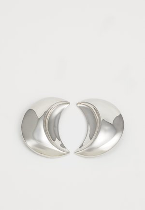 Brincos em forma de crescente prateada com um acabamento polido, apresentando curvas suaves e superfícies reflexivas, criando um design elegante e moderno.