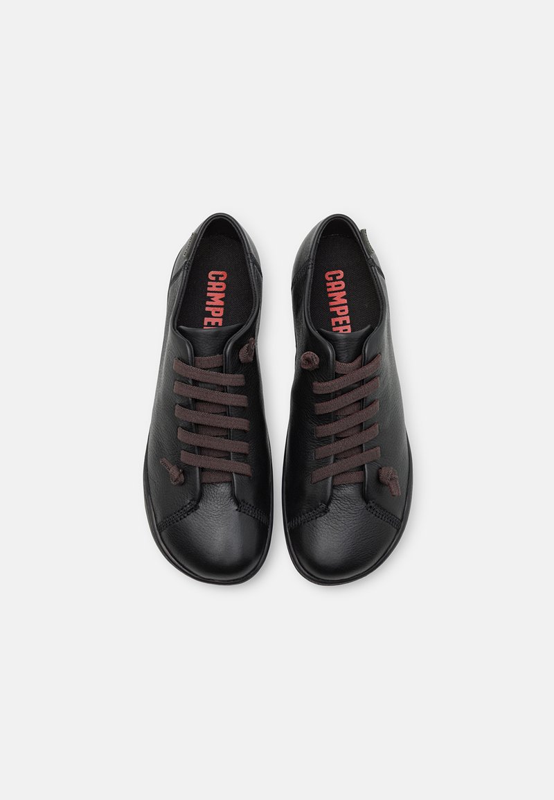 Svarta läderskor med rund tå, försedd med mörkbruna snörningar och röd "CAMPPER"-logotyp på innersulorna. Ren design.