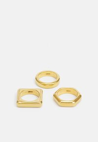 Set di tre anelli in oro: uno rotondo, uno quadrato e uno esagonale. Superficie liscia con una finitura lucida, che mette in mostra forme geometriche.
