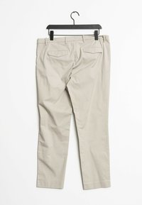 Pantalones beige con corte recto, hechos de tela de algodón. Presenta dos bolsillos traseros y una cinturilla. Cuélgate en un gancho de plástico negro.