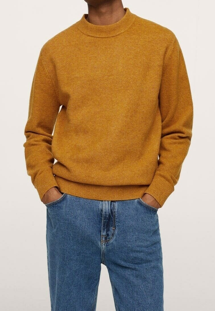 Musztardowy sweter z dzianiny, z okrągłym dekoltem, ribbowymi mankietami i dołem. W połączeniu z jasnoniebieskimi dżinsami, prezentującymi luźny krój.