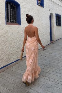 Pfirsichfarbendes Maxi-Kleid mit Blumenstickerei, offenem Rücken, volantsaum und lockerer Passform, kombiniert mit einer geflochtenen Clutch und beigen Schuhen.